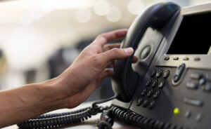close up employee man hand touching handset of telephone on desk for contact customer or receiving call , hotline concept