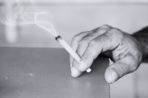 Rolled cannabis cigarette in senior man hand.Burning Mariuana joint using in medical purpose. Spliff with copy space.Black and white photo