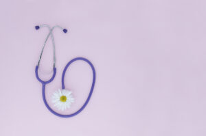Stethoscope, white flower on pink background with copy space. Medical flat lay. International Nurse's Day.