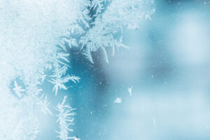 Beautiful frost pattern on a window glass over blurred blue outdoor background, macro photo
