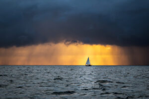 Lonely sailing yacht in the ocean at the approaching storm and raining clouds at sunrise, English channel, near French shores