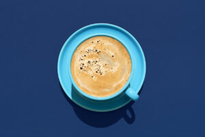 Above view with a cup of coffee minimalist on a blue table. Hot coffee in a blue cup in bright light.