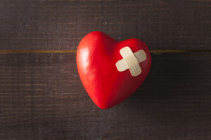 Red broken heart with a band-aid on a wooden background"n