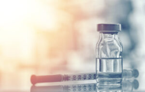 Closeup of medicine vial or flu, measles vaccine bottle with syringe and needle for immunization on vintage medical background, medicine and drug concept