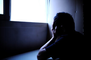 Sillhouette of a sad and problematic young man sitting next to a window light source. Mental health, depression and stress concept