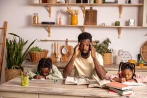 Tired father and children gathering around table doing kid's homework at home