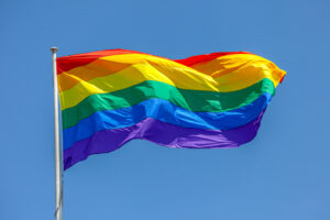 A large rainbow flag waving in the wind against a blue sky