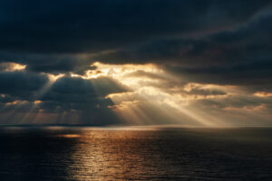 Orange sunset with sun rays through dark clouds over the sea with reflection