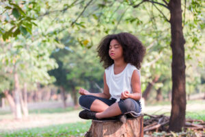 African American little girl doing meditate yoga asana with eyes closed outdoor in park. Kids girl practicing doing yoga outdoor