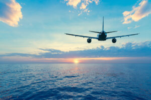 Flying of the passenger plane above the sea surface at sunset time.