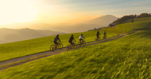 AERIAL: Biking friends on a scenic bike ride through hilly Slovenian countryside. Group of young mountain bikers riding along a hilltop mountain trail with breathtaking views on sunny autumn morning.