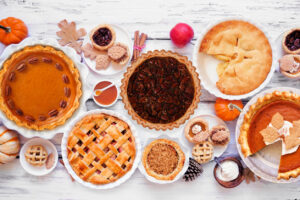 Homemade autumn pie table scene. Top down view on a white wood background. Variety of apple, pumpkin and pecan pies.