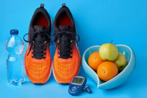 Orange sneakers, glucometer, bottle of drinking water and fruits on blue background. Concept of healthy lifestyle to maintain normal blood glucose levels. Blood glucose control