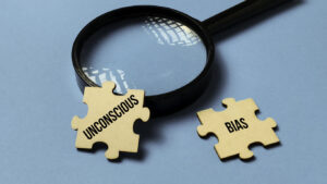Examining Unconscious Bias: Magnifying Glass Focuses on Two Puzzle Pieces on a Blue Background