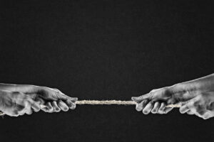 Hand in Black and White Pulling Rope to Opposite Sides, Paper Textured Black Background with Copy Space