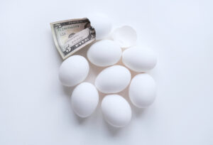 Group of white eggs with five dollar bill in broken one representing egg price inflation due to Avian flu epidemic.